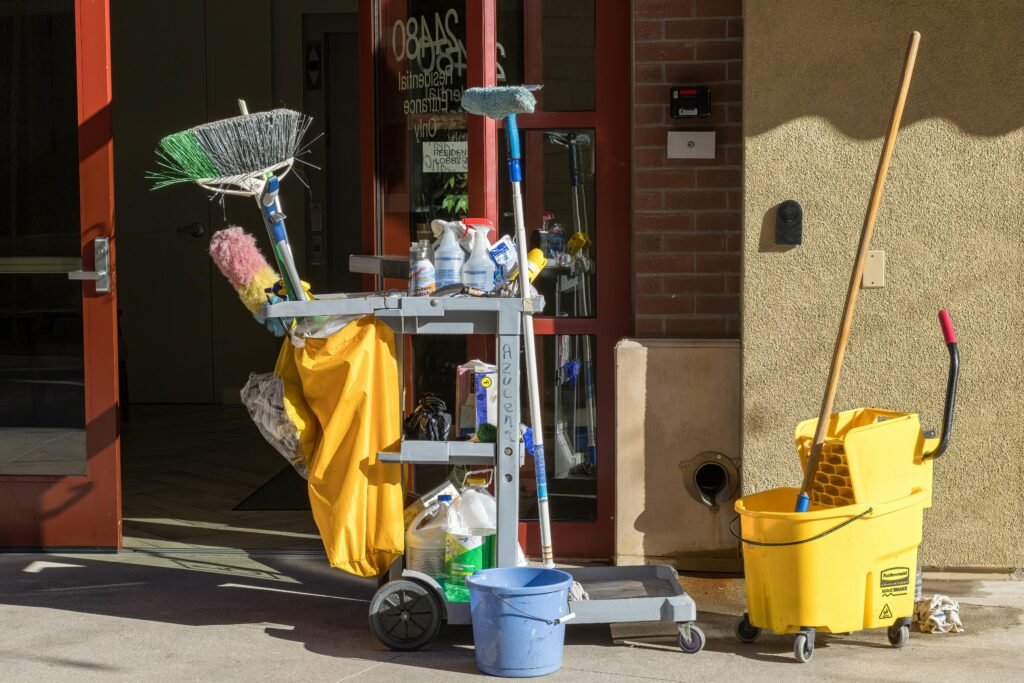 Cleaning supplies and tools outside a building entrance bathed in sunlight.