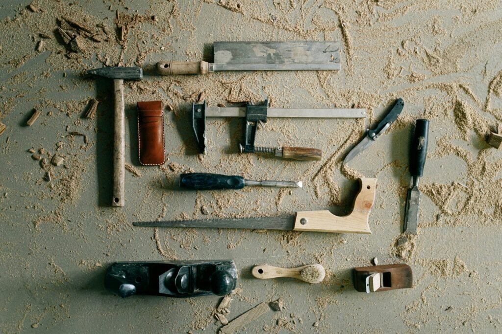 A collection of vintage woodworking tools on a sandy workbench, evoking a rustic and crafted feel.
